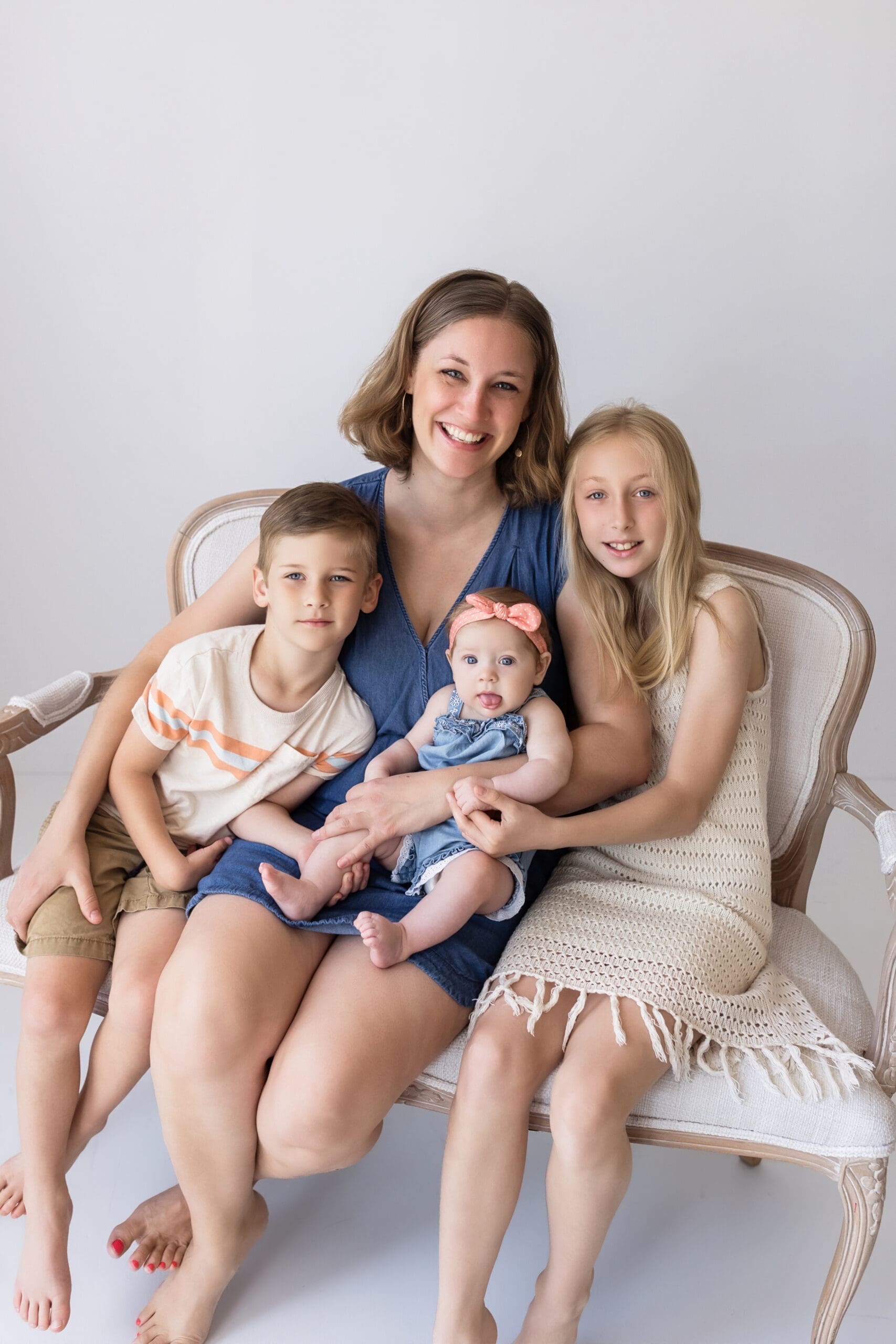 Mother with three children sitting together on a bench in an all white studio during a natural family photography session