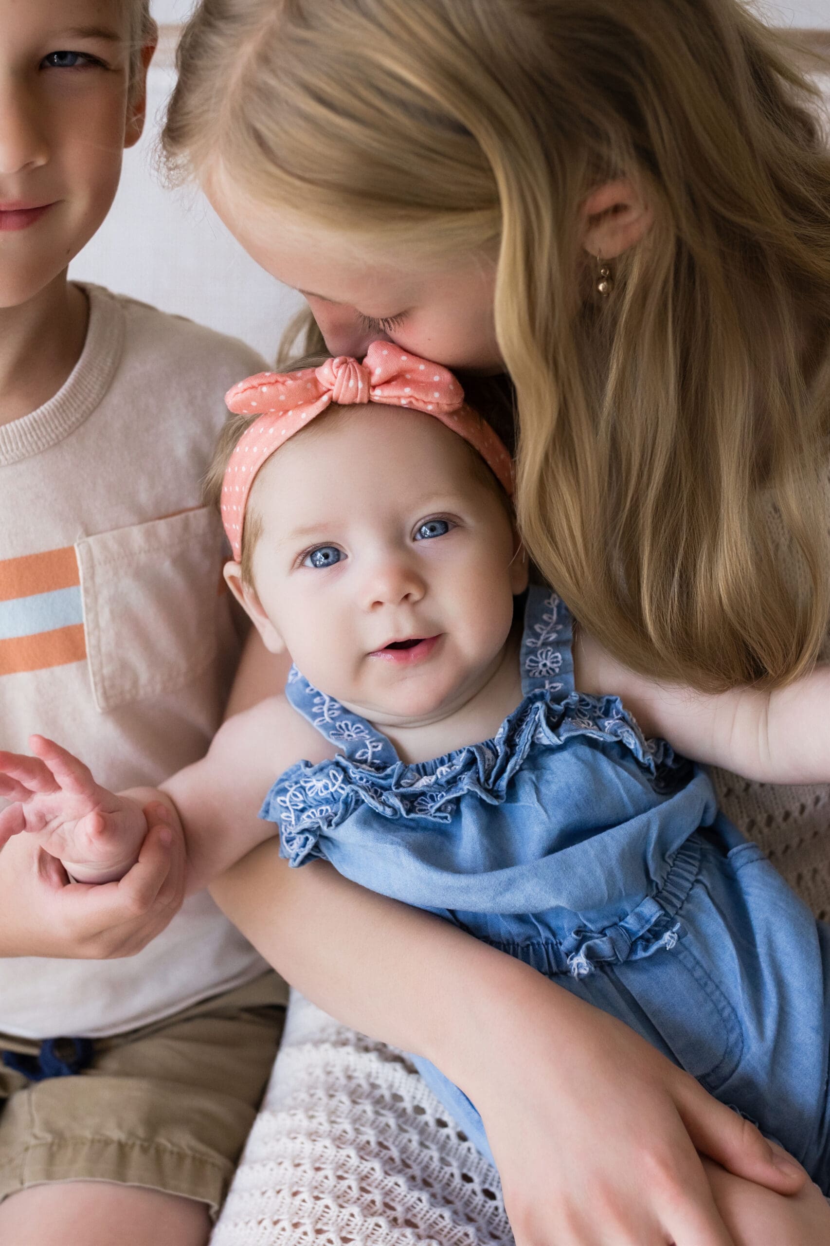 Newborn baby girl being gently held by her brother and sister during a natural family photography session