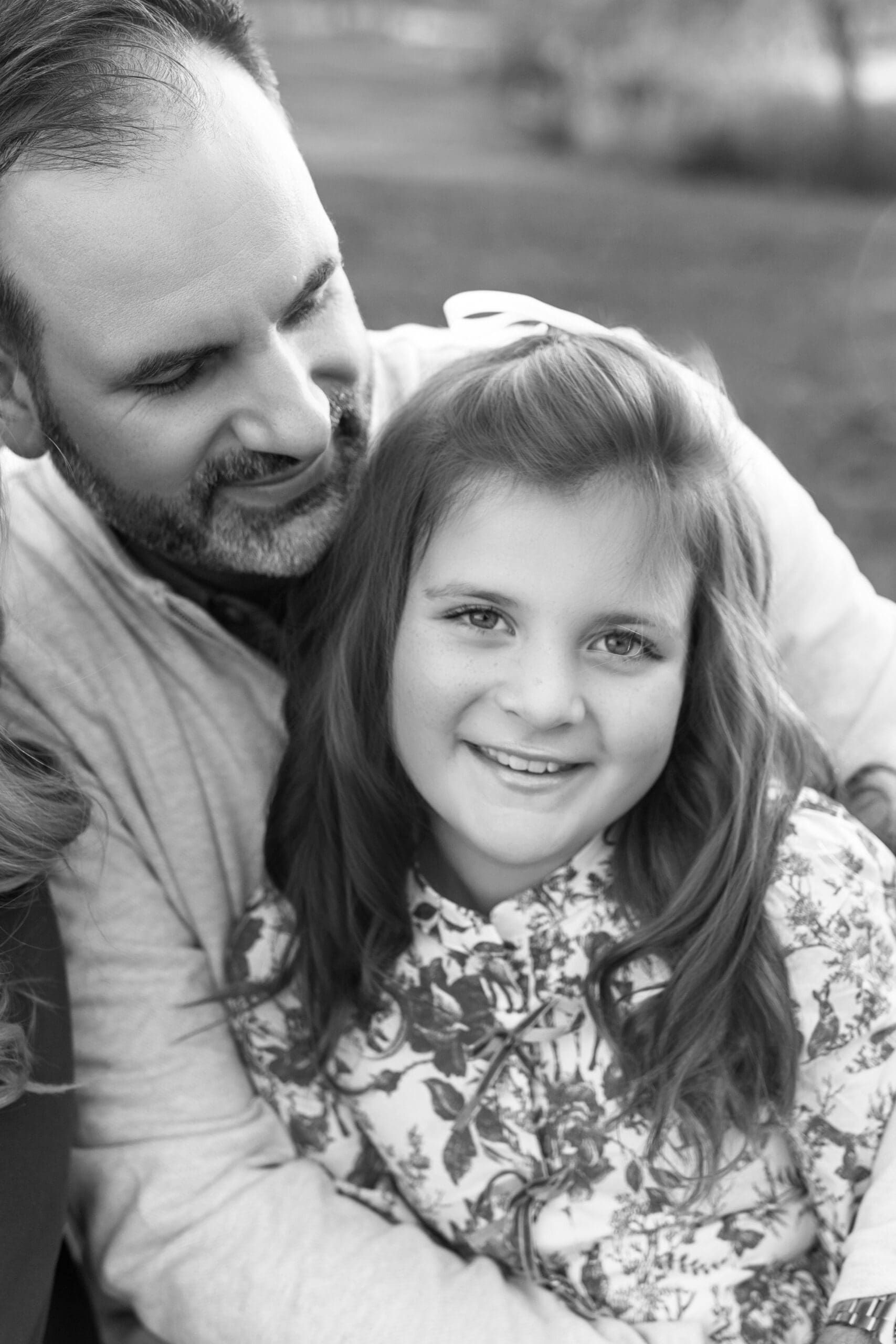 Father looking down and smiling at his little girl in a park during a family photography session